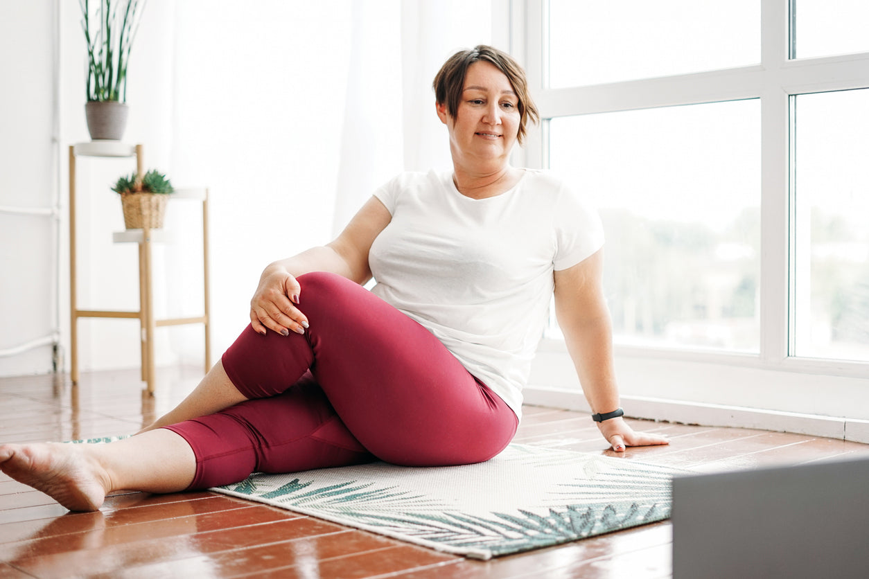 A woman stretching at home while watching instruction on a laptop